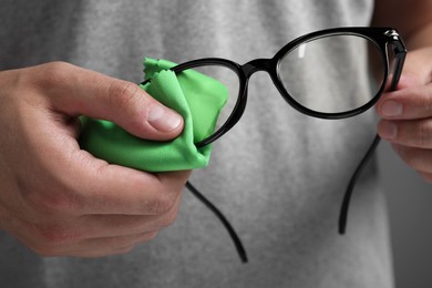 Photo of Man wiping glasses with microfiber cloth on grey background, closeup