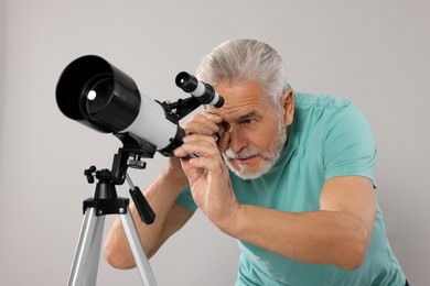 Senior astronomer looking at stars through telescope on grey background