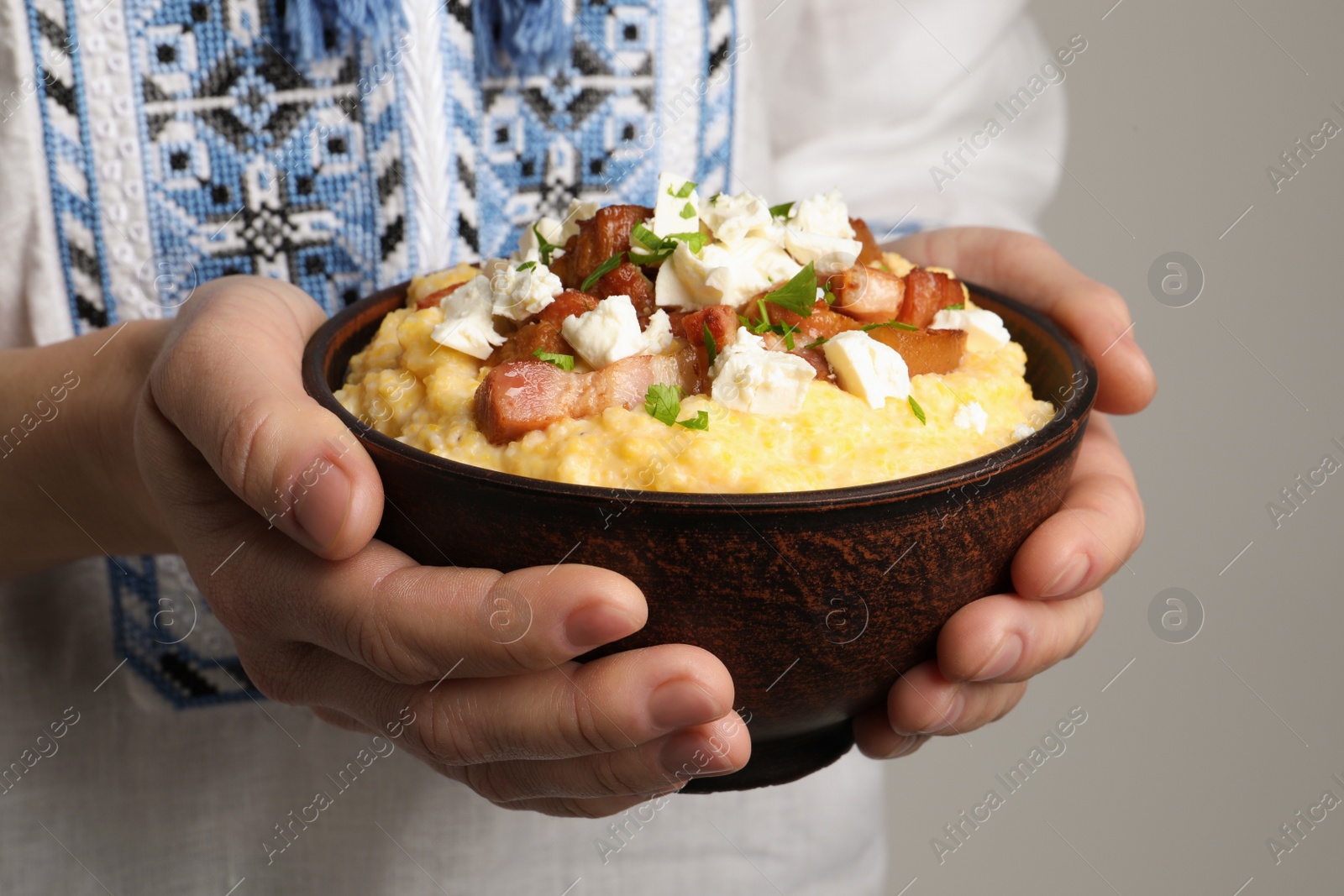 Photo of Woman holding bowl of delicious traditional Ukrainian banosh on grey background, closeup