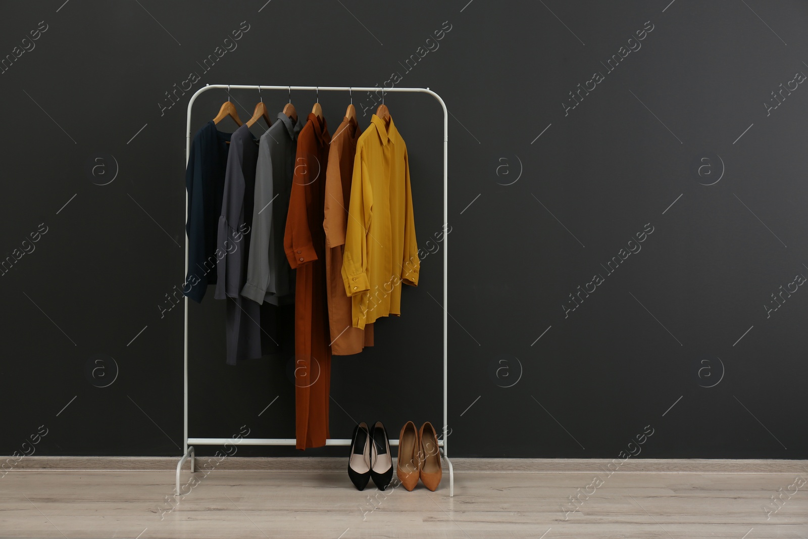 Photo of Rack with stylish clothes near black wall. Space for text