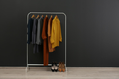 Photo of Rack with stylish clothes near black wall. Space for text