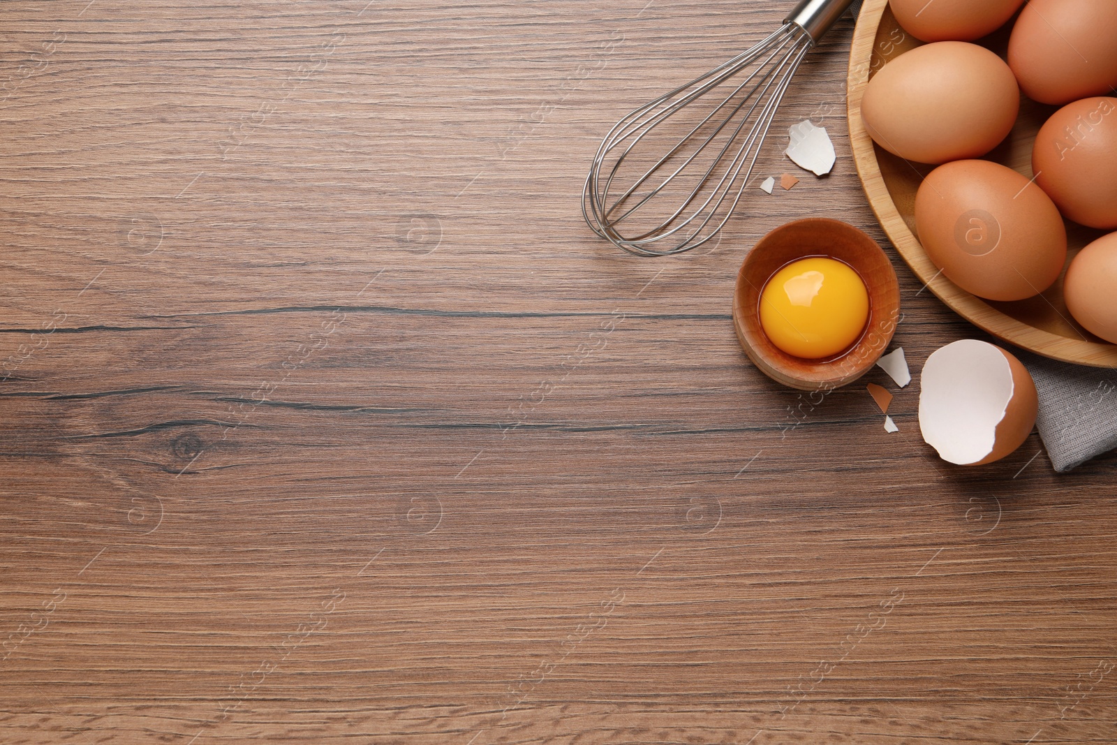 Photo of Chicken eggs, bowl with raw yolk and whisk on wooden table, flat lay. Space for text