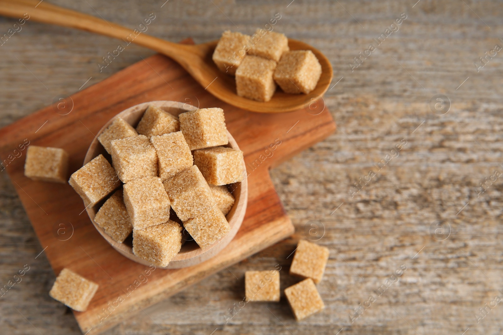 Photo of Bowl and spoon with brown sugar cubes on wooden table, above view. Space for text