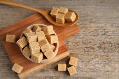 Photo of Bowl and spoon with brown sugar cubes on wooden table, above view. Space for text