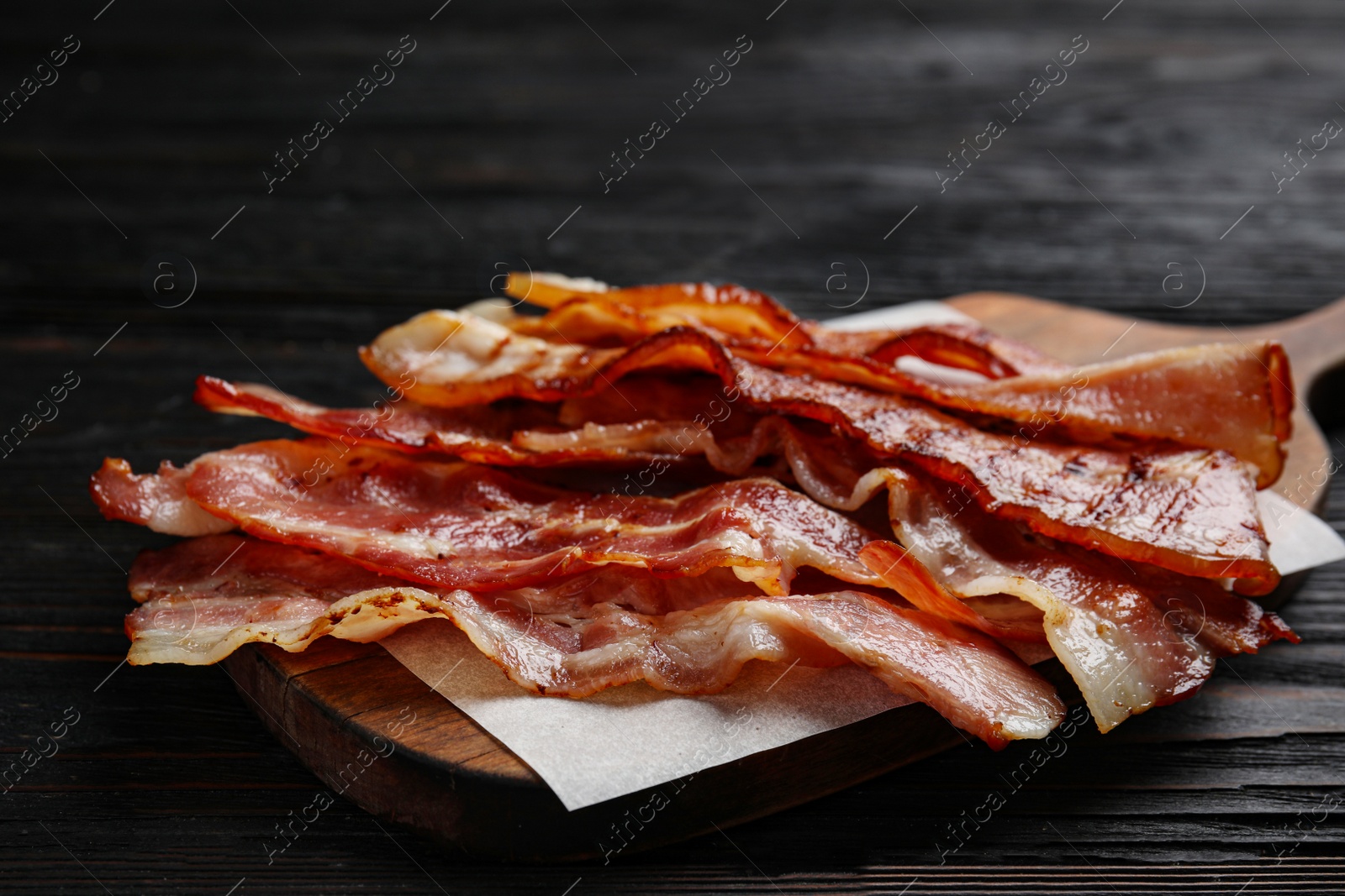 Photo of Slices of tasty fried bacon on black wooden table, closeup