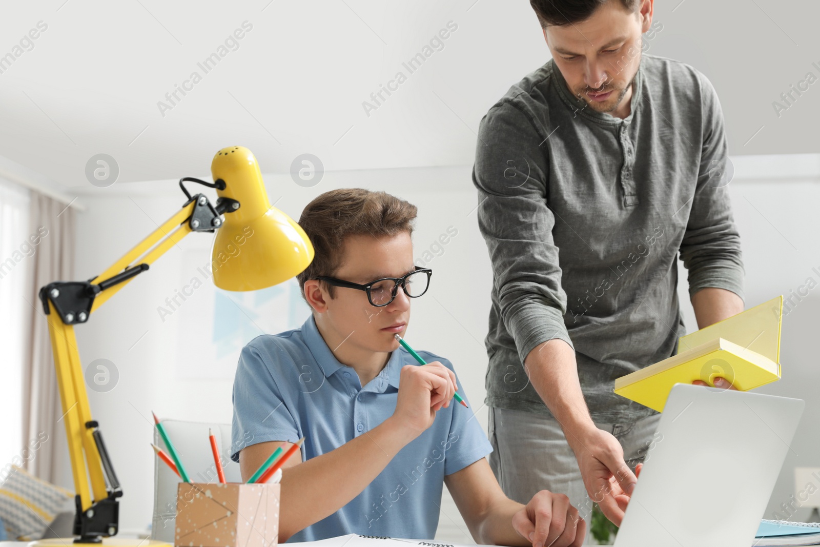 Photo of Father helping his teenager son with homework indoors