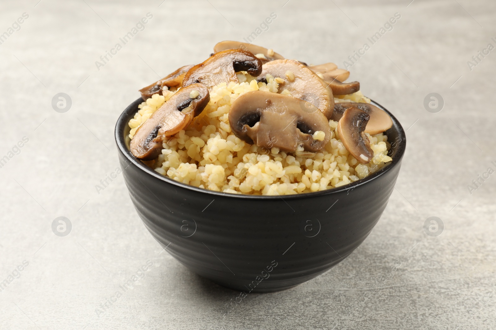 Photo of Delicious bulgur with mushrooms in bowl on gray table, closeup