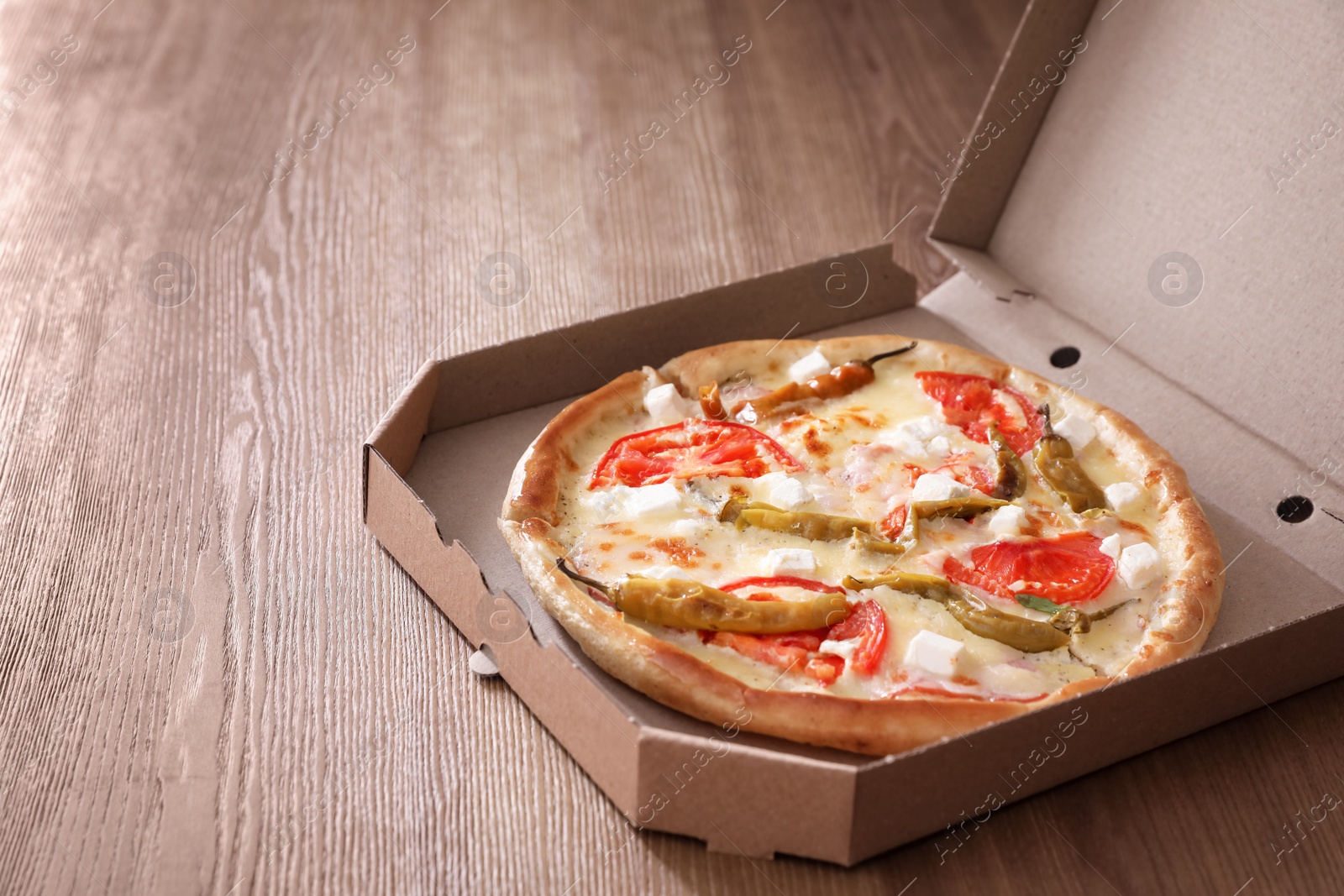 Photo of Cardboard box with tasty pizza on wooden table