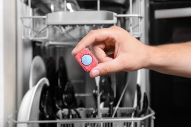 Woman putting detergent tablet into open dishwasher in kitchen, closeup