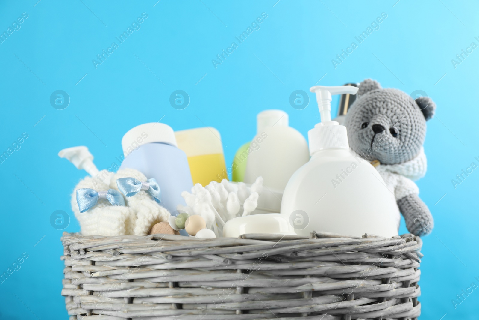 Photo of Wicker basket full of different baby cosmetic products, bathing accessories and toy on light blue background, closeup
