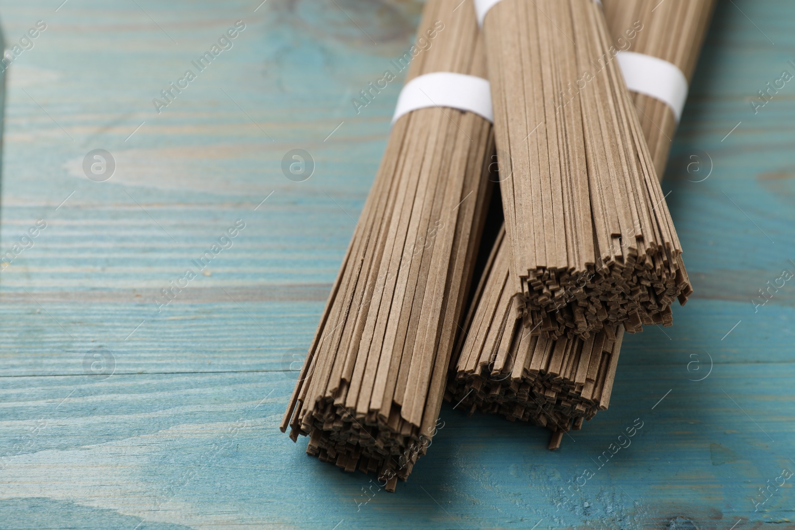 Photo of Uncooked buckwheat noodles (soba) on light blue wooden table, closeup. Space for text