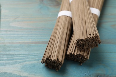 Photo of Uncooked buckwheat noodles (soba) on light blue wooden table, closeup. Space for text