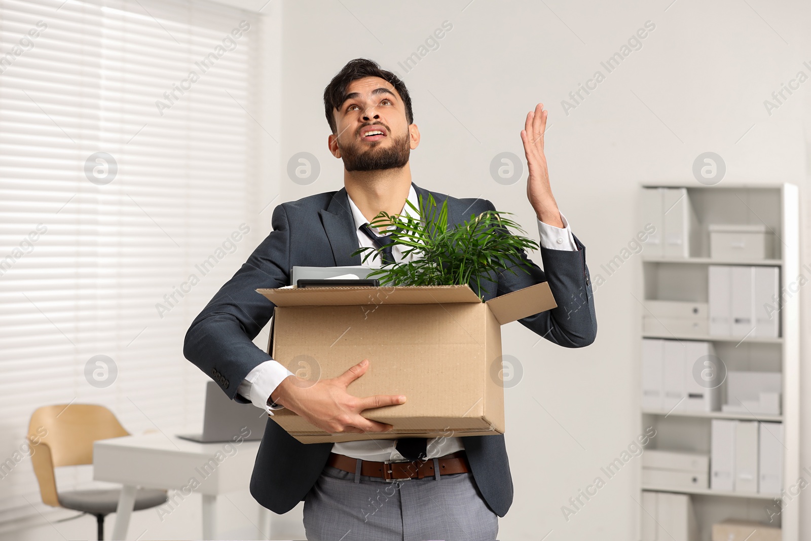 Photo of Unemployment problem. Frustrated man with box of personal belongings in office