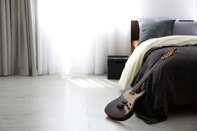 Photo of Electric guitar near bed in modern teenager's room interior, space for text