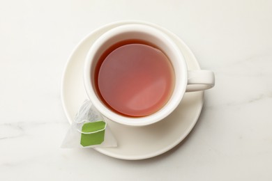 Tea bag and cup of hot beverage on white table, top view