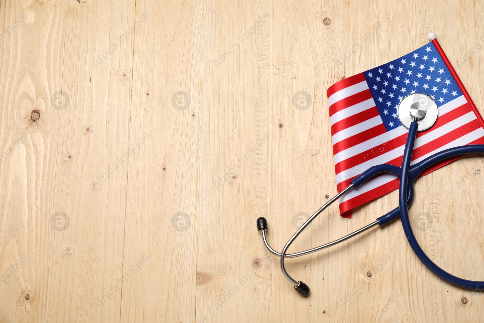 Photo of Stethoscope and USA flag on wooden table, top view. Space for text