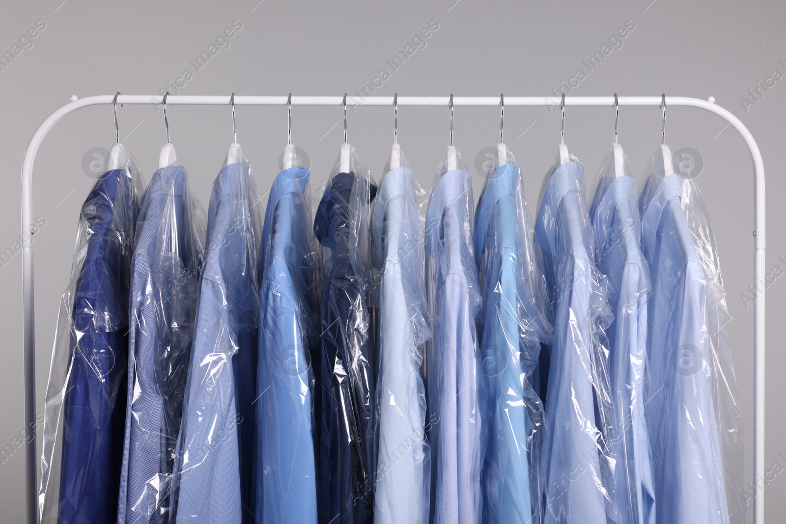 Photo of Dry-cleaning service. Many different clothes in plastic bags hanging on rack against grey background