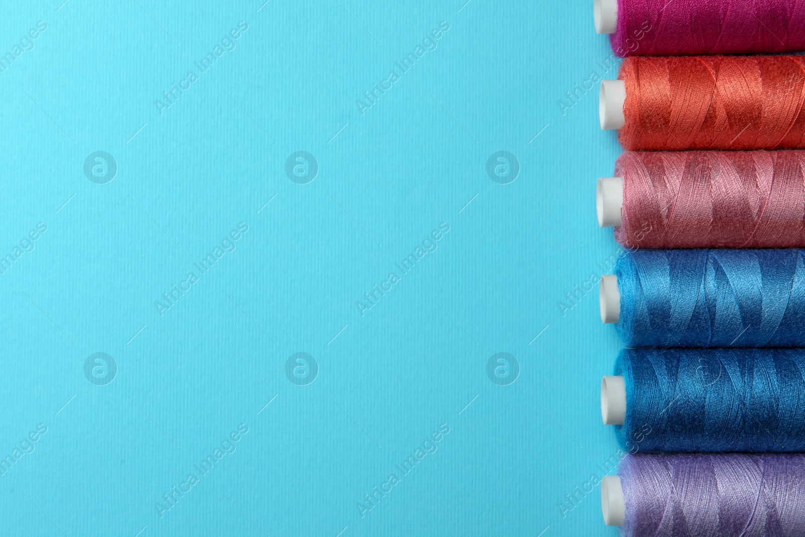 Photo of Set of different colorful sewing threads on light blue background, flat lay. Space for text