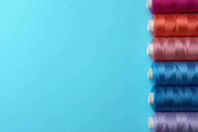 Photo of Set of different colorful sewing threads on light blue background, flat lay. Space for text