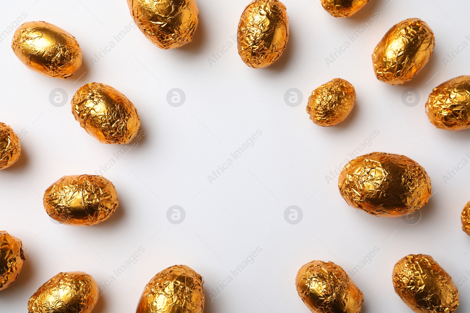 Photo of Frame of chocolate eggs wrapped in golden foil on white background, flat lay. Space for text