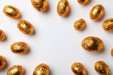 Frame of chocolate eggs wrapped in golden foil on white background, flat lay. Space for text