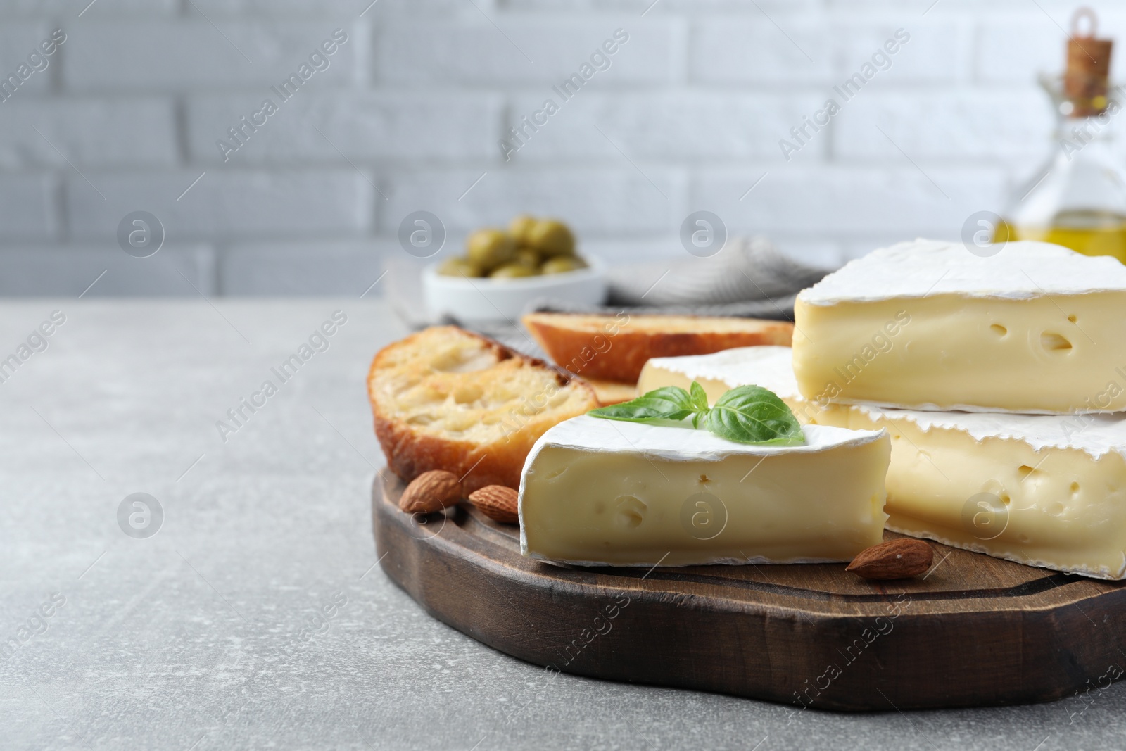 Photo of Tasty brie cheese with basil, bread and almonds on grey table, space for text