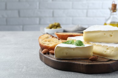 Photo of Tasty brie cheese with basil, bread and almonds on grey table, space for text