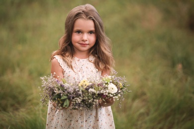 Cute little girl holding wreath made of beautiful flowers in field