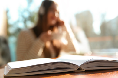 Book on table in cafe and woman with headphones on background. Audiobook concept