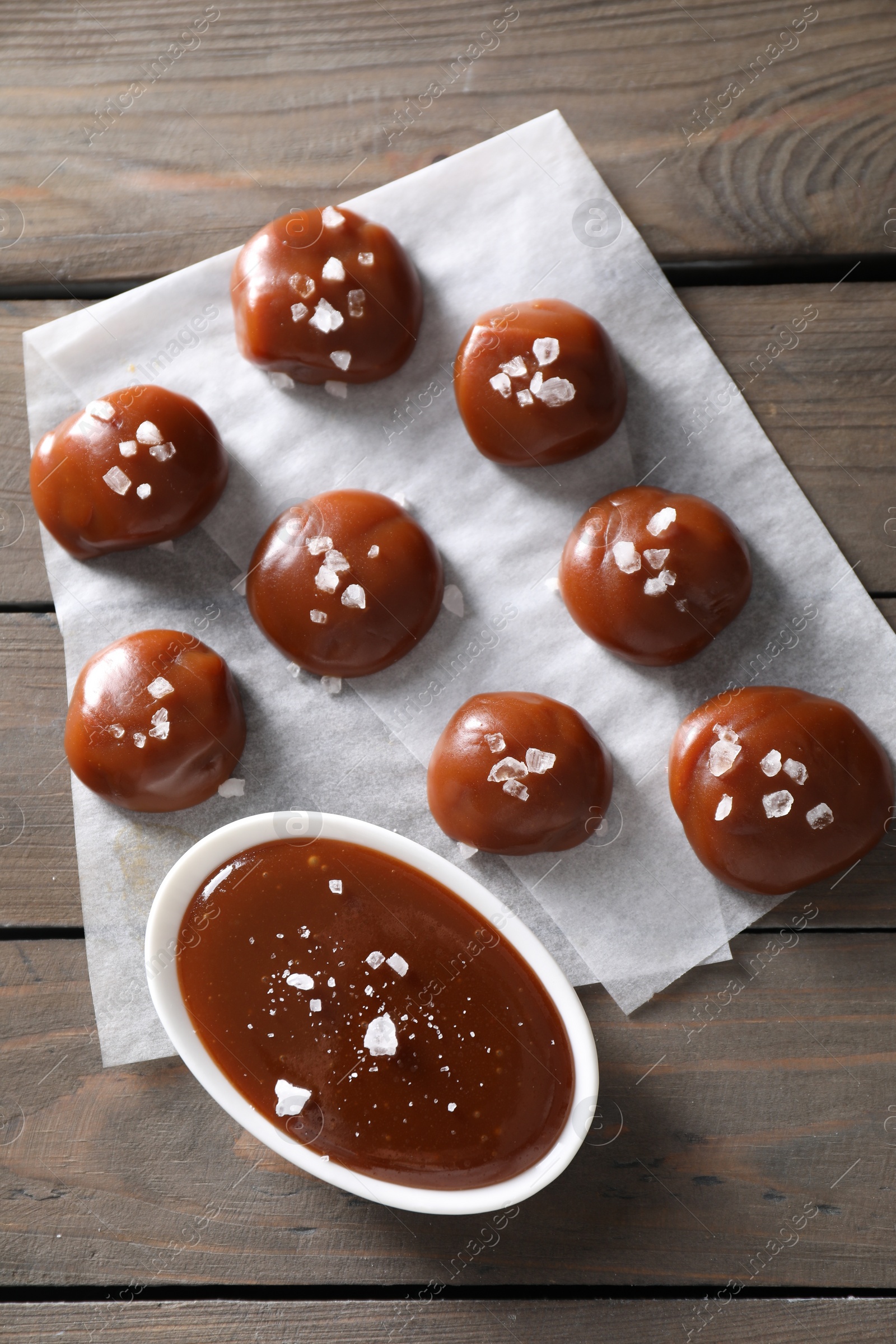 Photo of Tasty candies, caramel sauce and salt on wooden table, top view