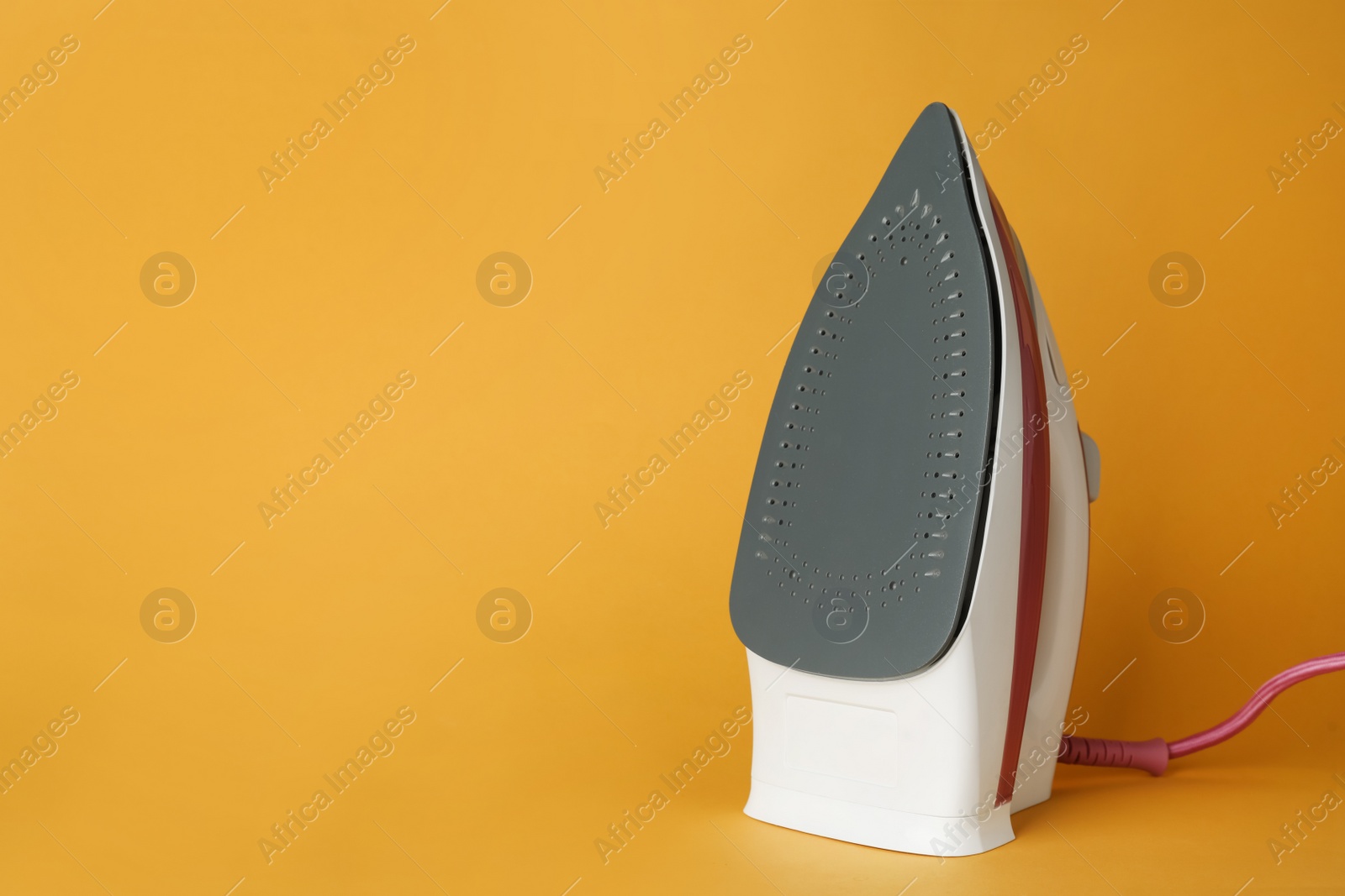 Photo of One modern iron on orange background, space for text. Home appliance