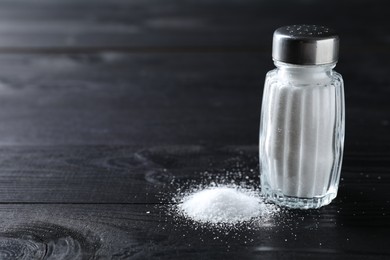 Organic salt in glass shaker on black wooden table, closeup. Space for text