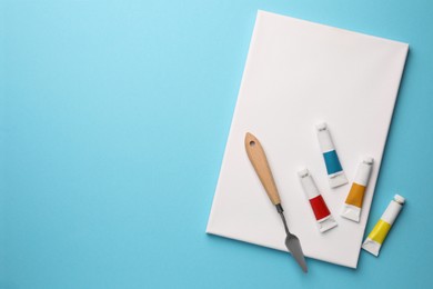 Photo of Blank canvas, tubes of oil paints and spatula on light blue background, flat lay. Space for text