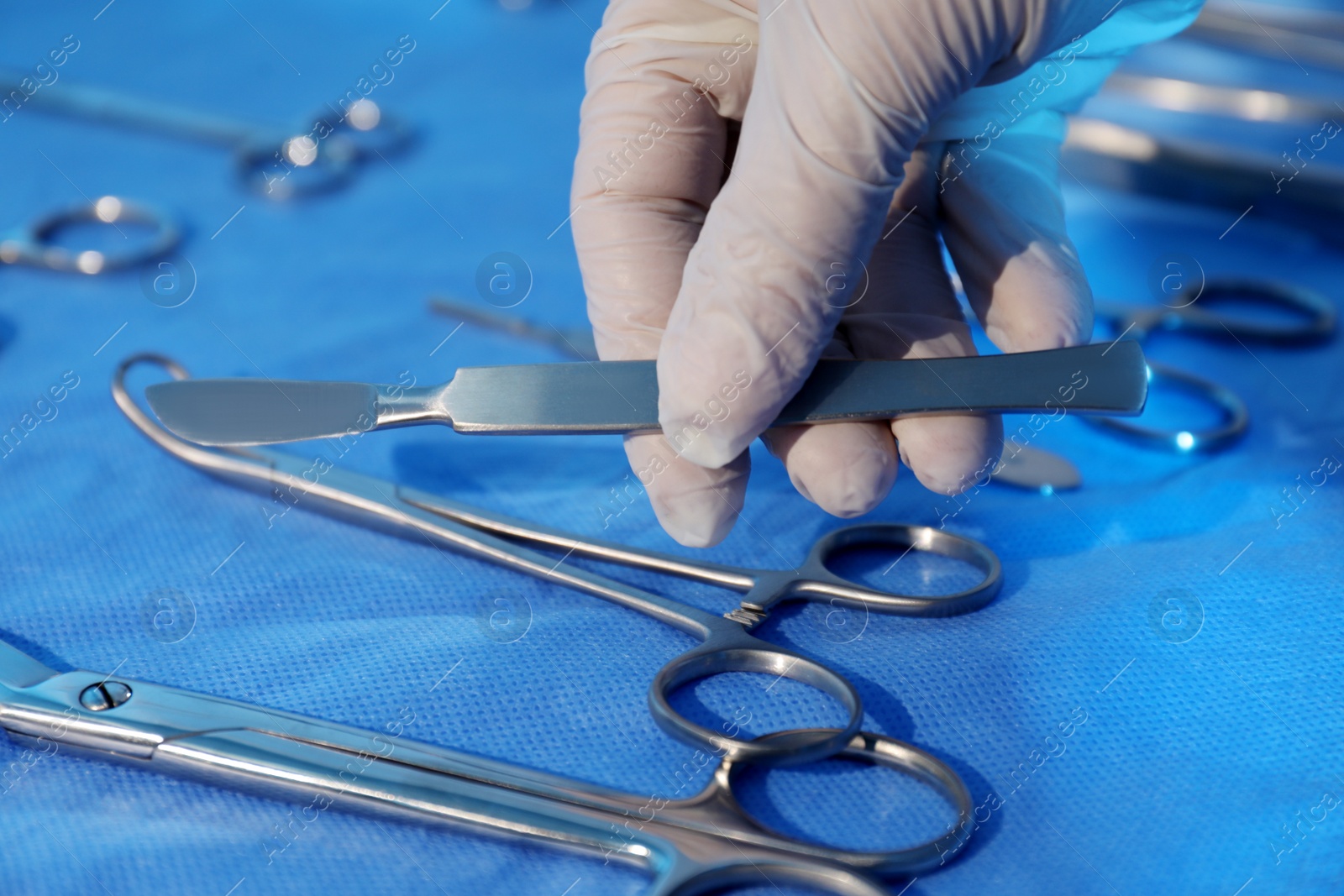 Photo of Doctor taking scalpel from table with different surgical instruments indoors, closeup