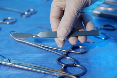 Photo of Doctor taking scalpel from table with different surgical instruments indoors, closeup