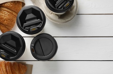 Coffee to go. Paper cups with tasty drink and croissants on white wooden table, flat lay. Space for text