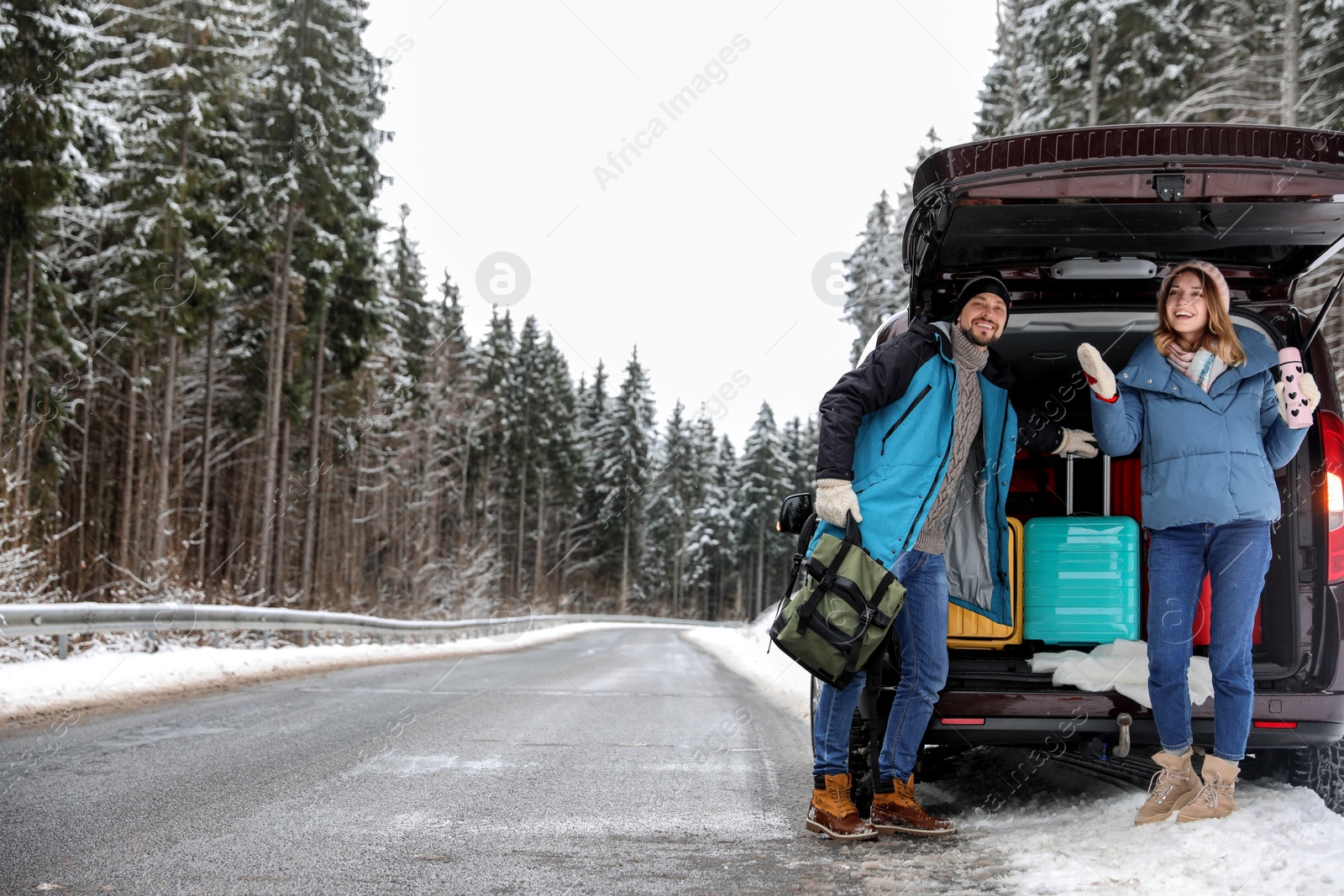 Photo of Couple near open car trunk full of luggage on road, space for text. Winter vacation