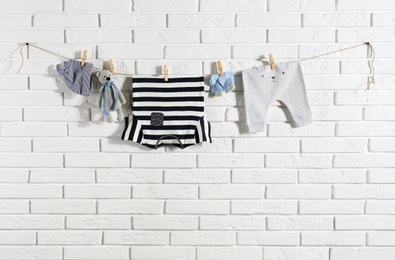 Baby clothes hanging on washing line near white brick wall