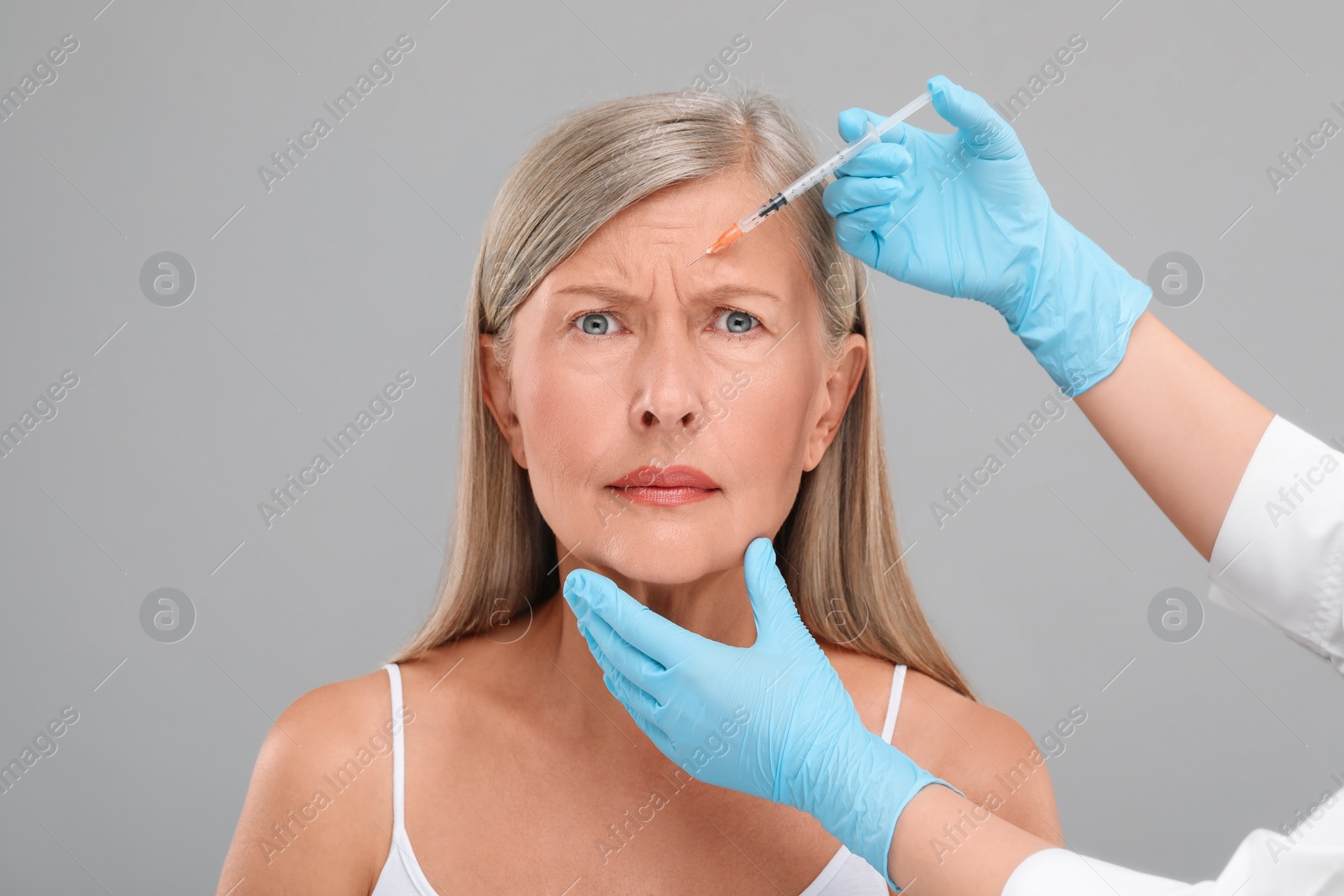 Photo of Doctor giving facial injection to senior woman on light grey background, closeup. Cosmetic surgery