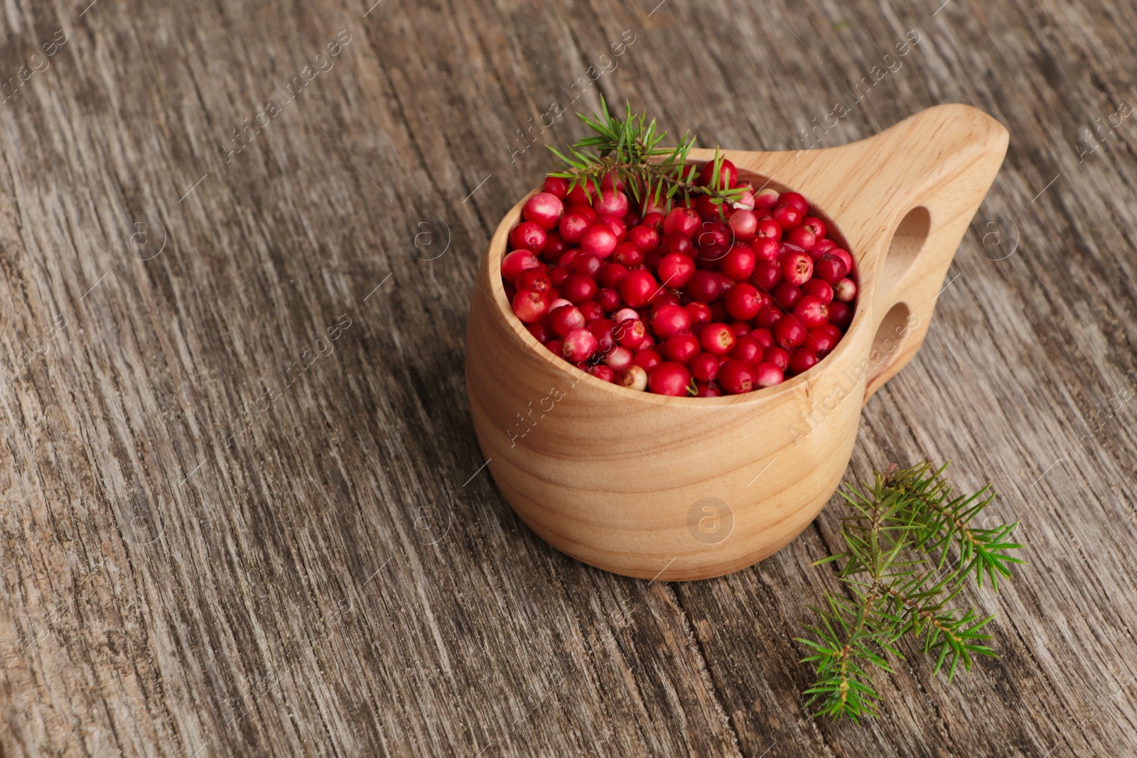 Photo of Cup with tasty ripe lingonberries and spruce twigs on wooden surface, space for text