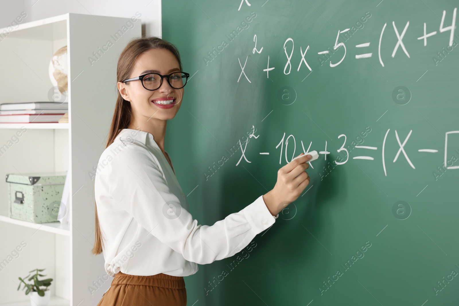 Photo of Young math’s teacher writing mathematical equations near chalkboard in classroom