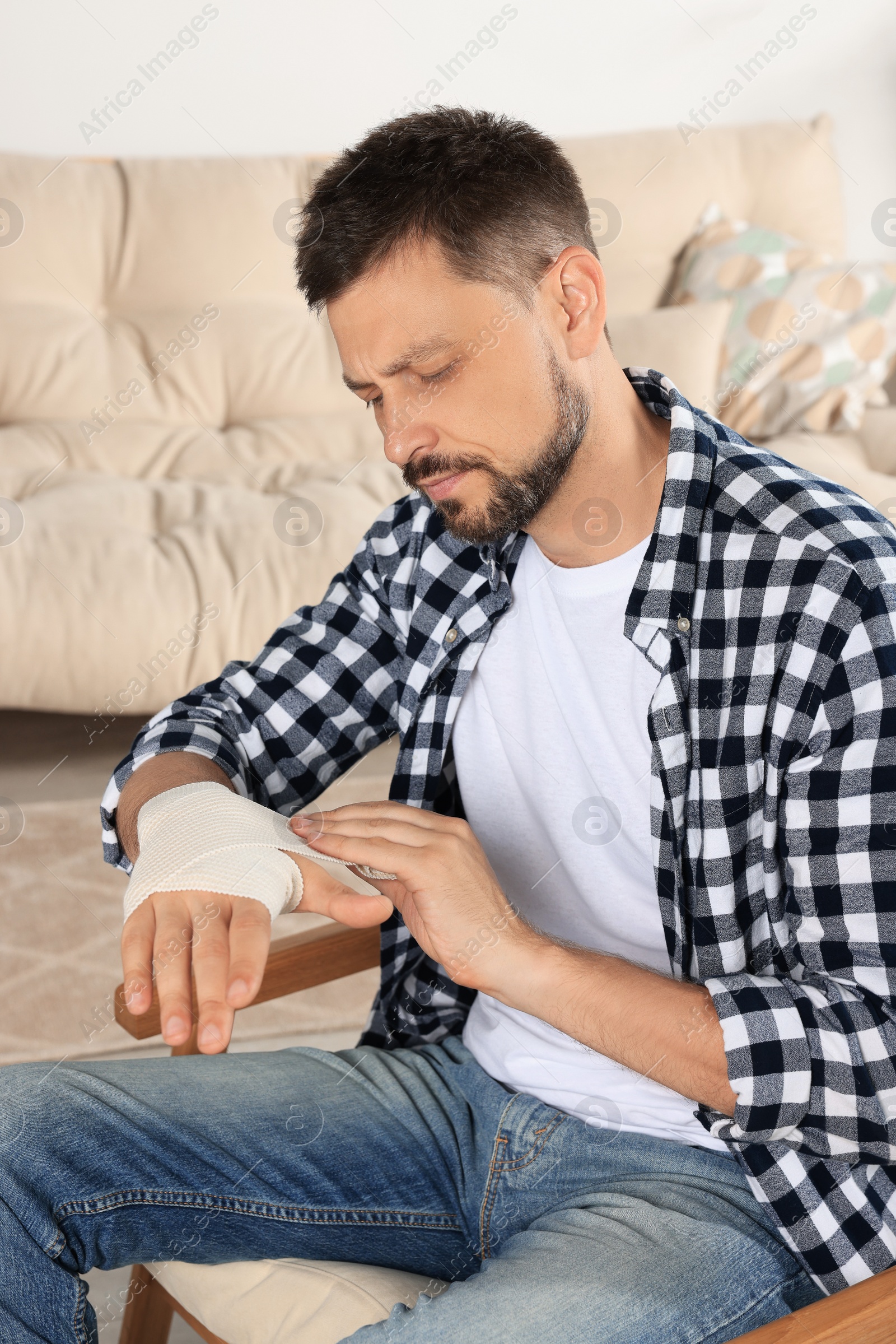 Photo of Man applying medical bandage onto hand at home