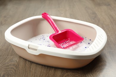 Photo of Cat litter tray with filler and scoop on wooden floor, closeup