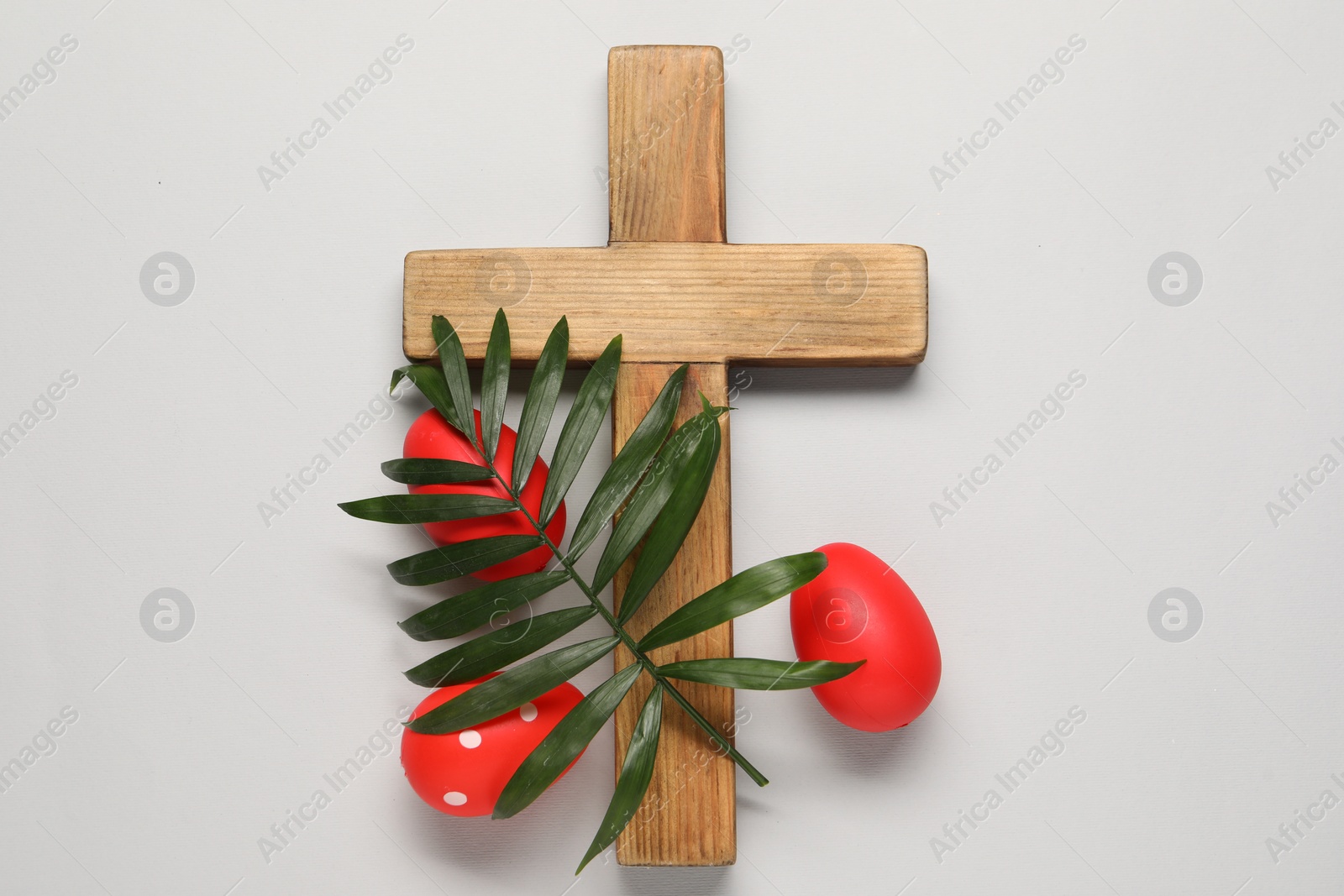 Photo of Wooden cross, painted Easter eggs and palm leaf on light grey background, flat lay