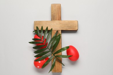 Photo of Wooden cross, painted Easter eggs and palm leaf on light grey background, flat lay