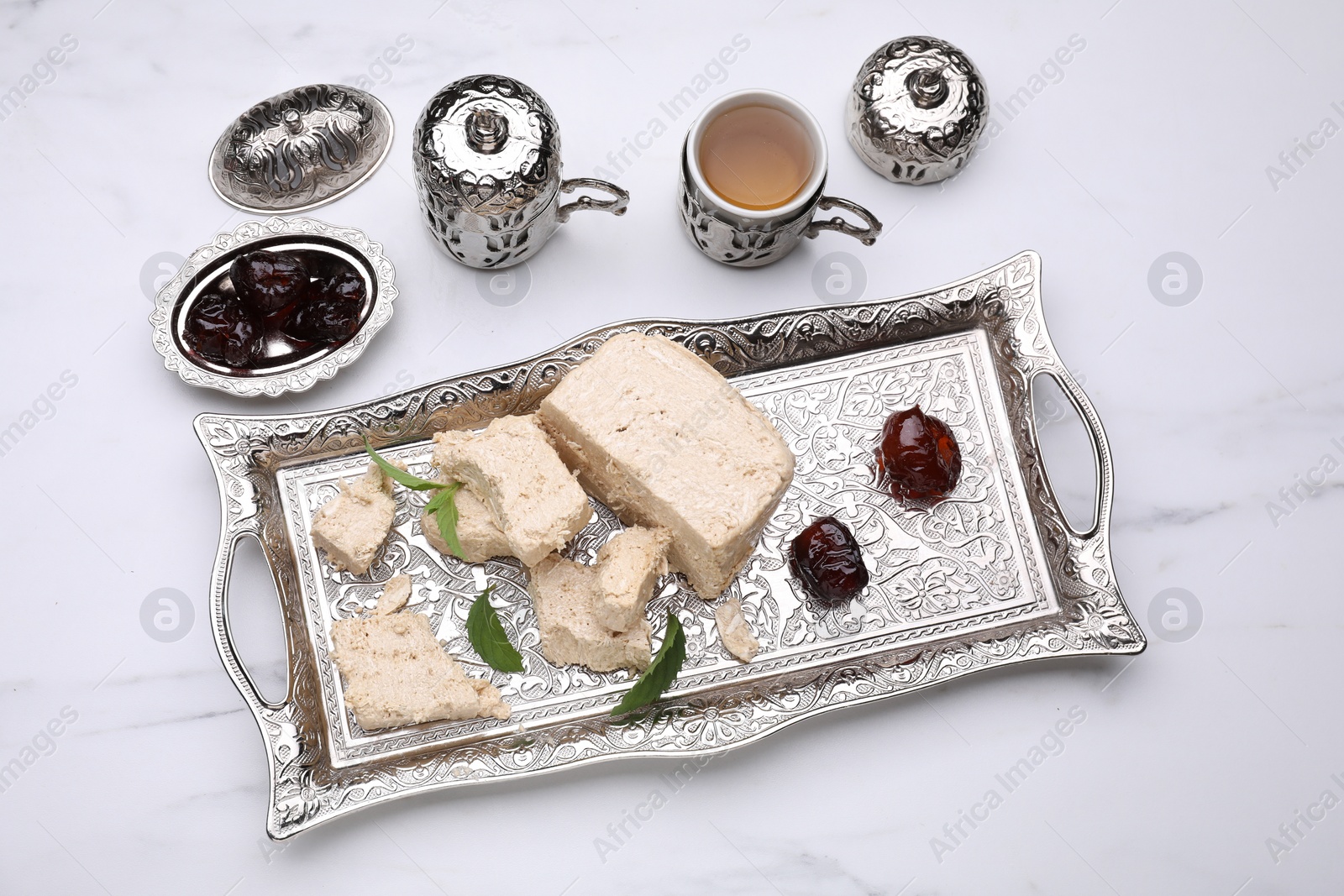 Photo of Pieces of tasty halva, tea, dates and mint leaves on white marble table, above view