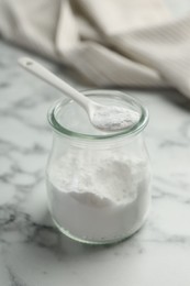 Photo of Baking powder in jar and spoon on white marble table, closeup