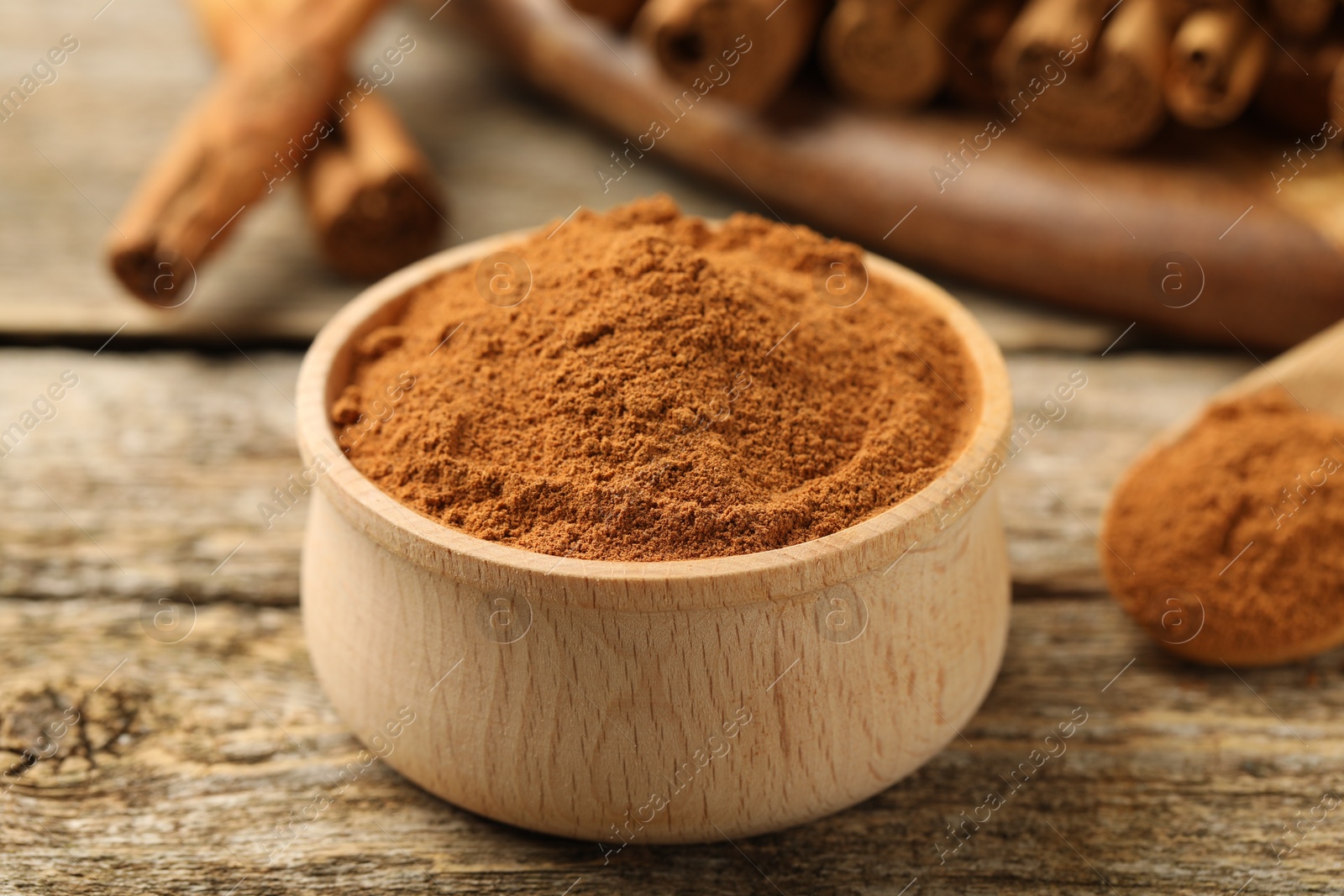 Photo of Bowl of cinnamon powder on wooden table, closeup