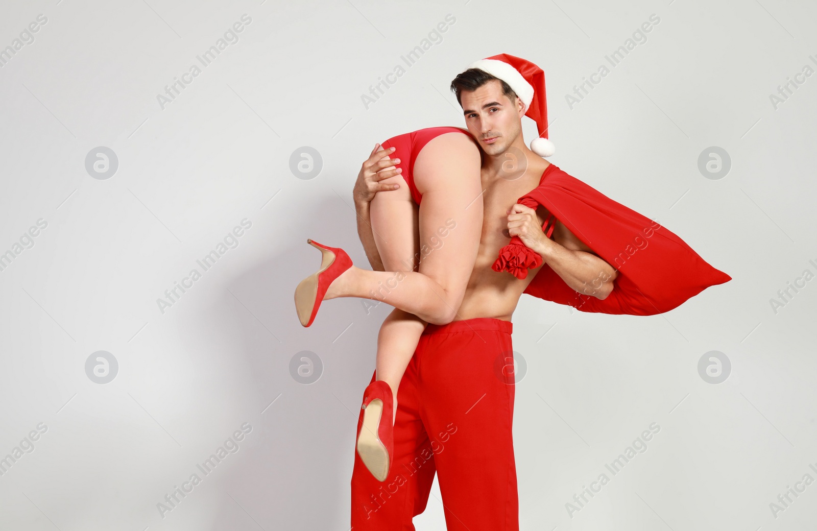 Photo of Attractive young Santa Claus with sexy woman on light background