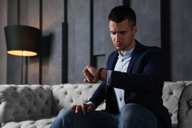 Photo of Handsome businessman checking time on sofa indoors. Luxury lifestyle